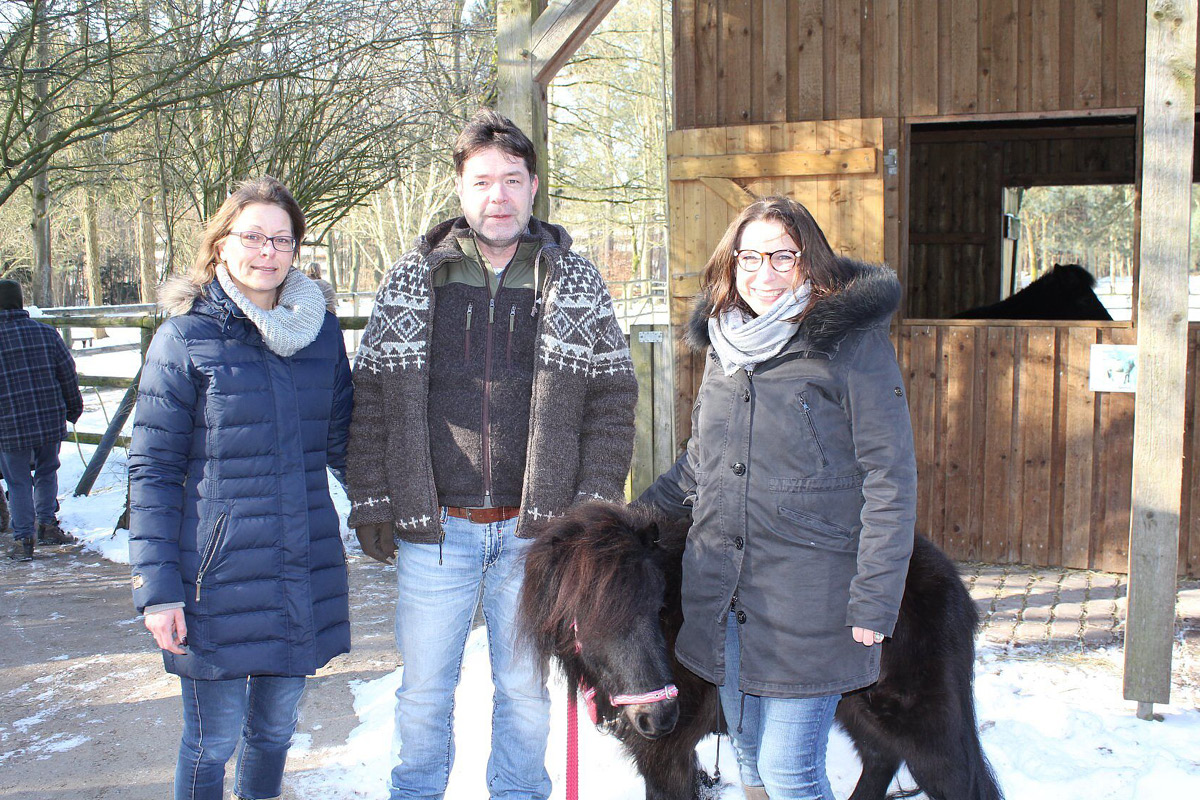 Drei Personen stehen mit einem Pony auf einem Hof