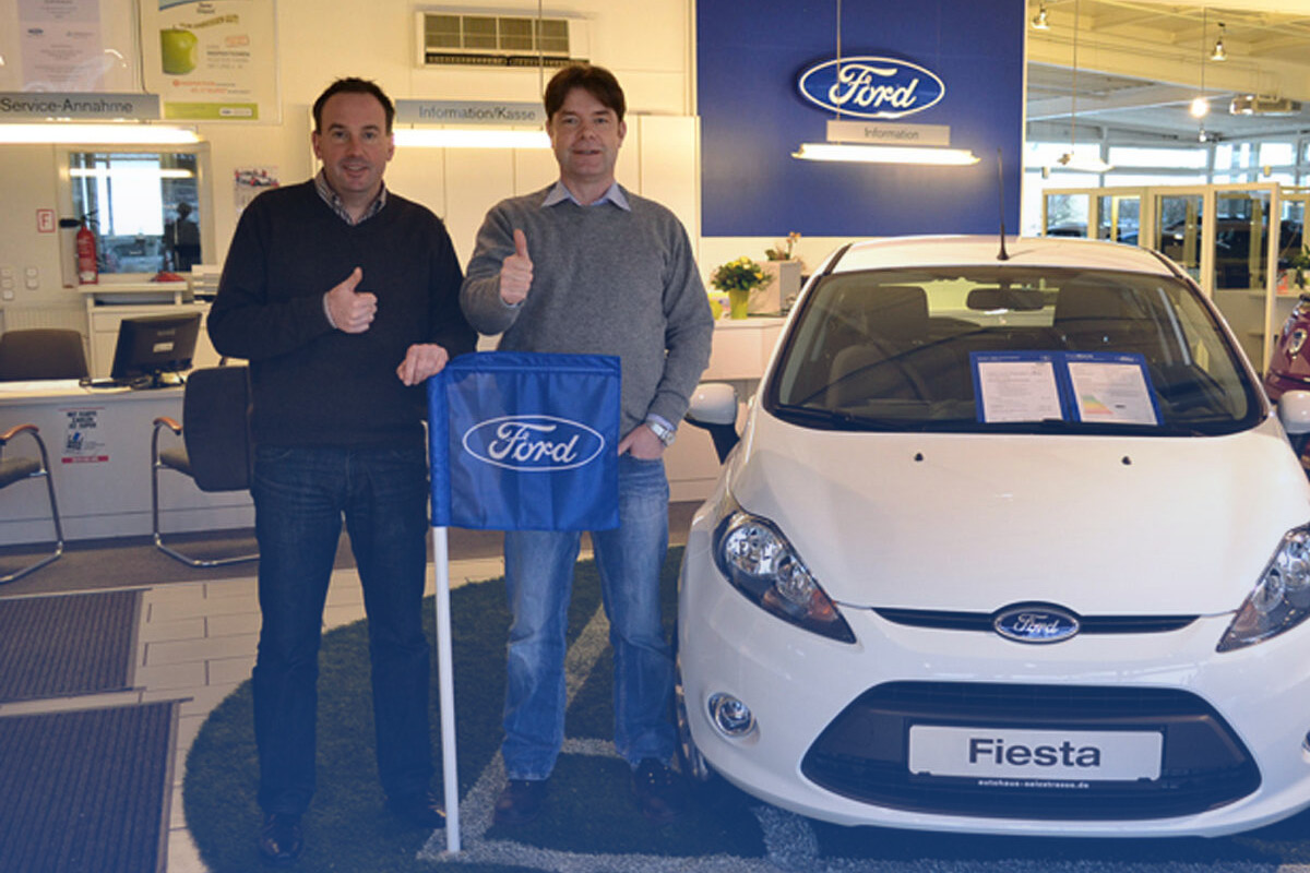 Zwei Menschen stehen neben einem Fahrzeug und zeigen einen Daumen nach oben